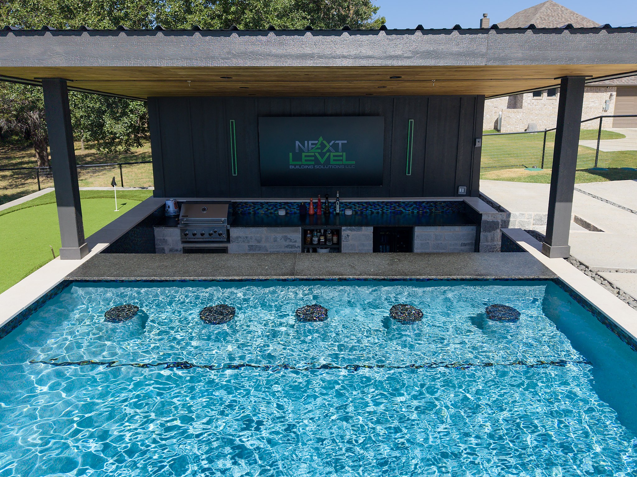 Swim up bar with submerged stools and a putting green beyond